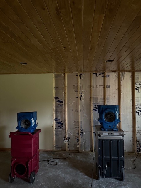 Basement under construction with water damage restoration equipment including red dehumidifier and blue air mover